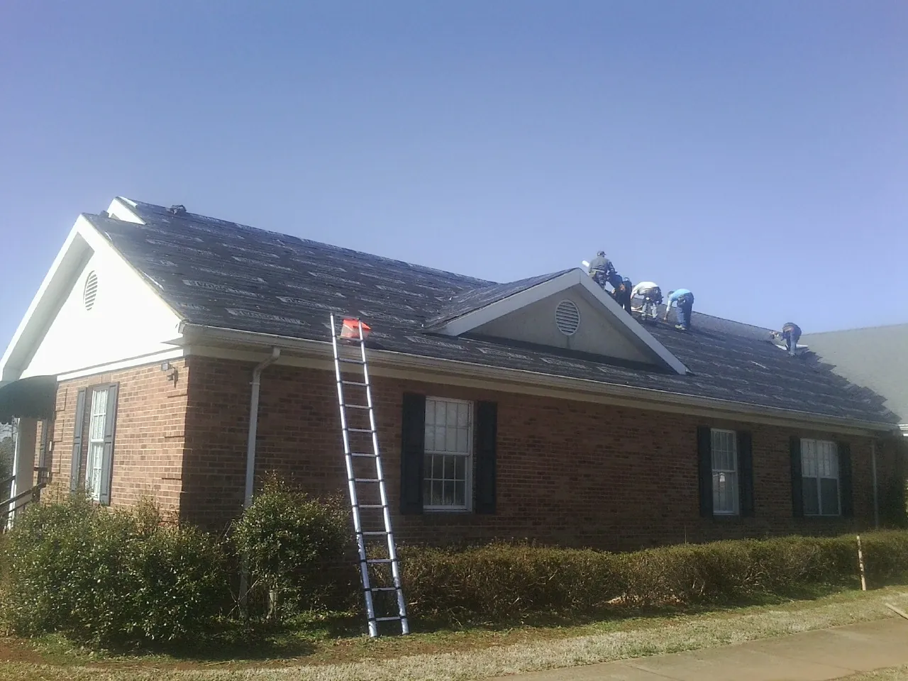 Crew tearing shingles off a brick ranch roof with a ladder set — Metal Roof Repair work by our crew in Millbrook