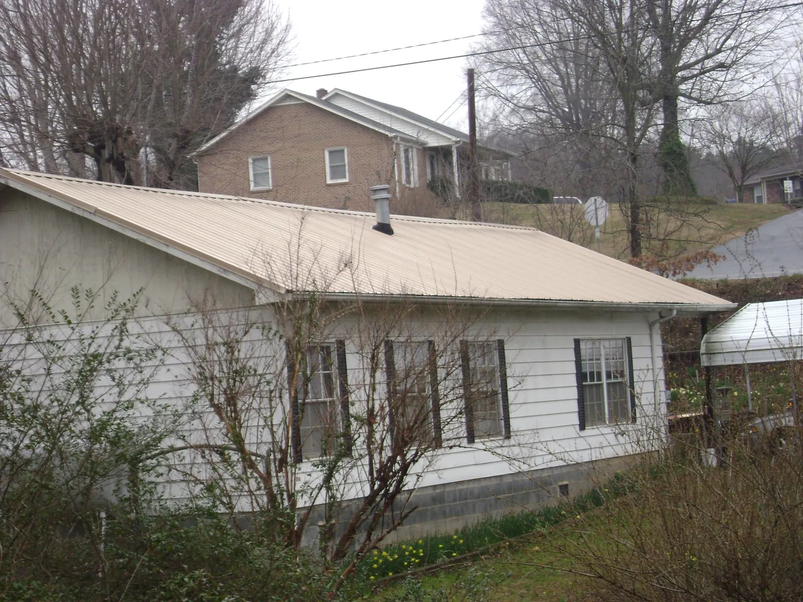Tan metal roof on a white sided house set into a hillside — Commercial Roofing by Roofing Brothers in Millbrook